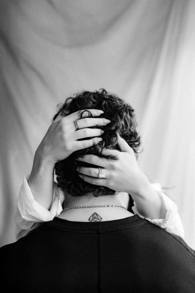 back of man's head, her hands intertwined in his hair showing his neck tattoo and her rings