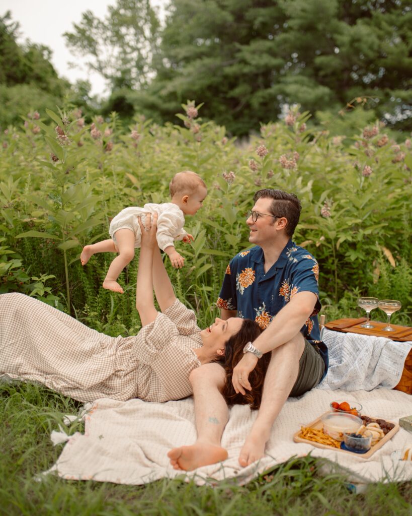 family on picnic blanket, mom raises child to give dad a kiss