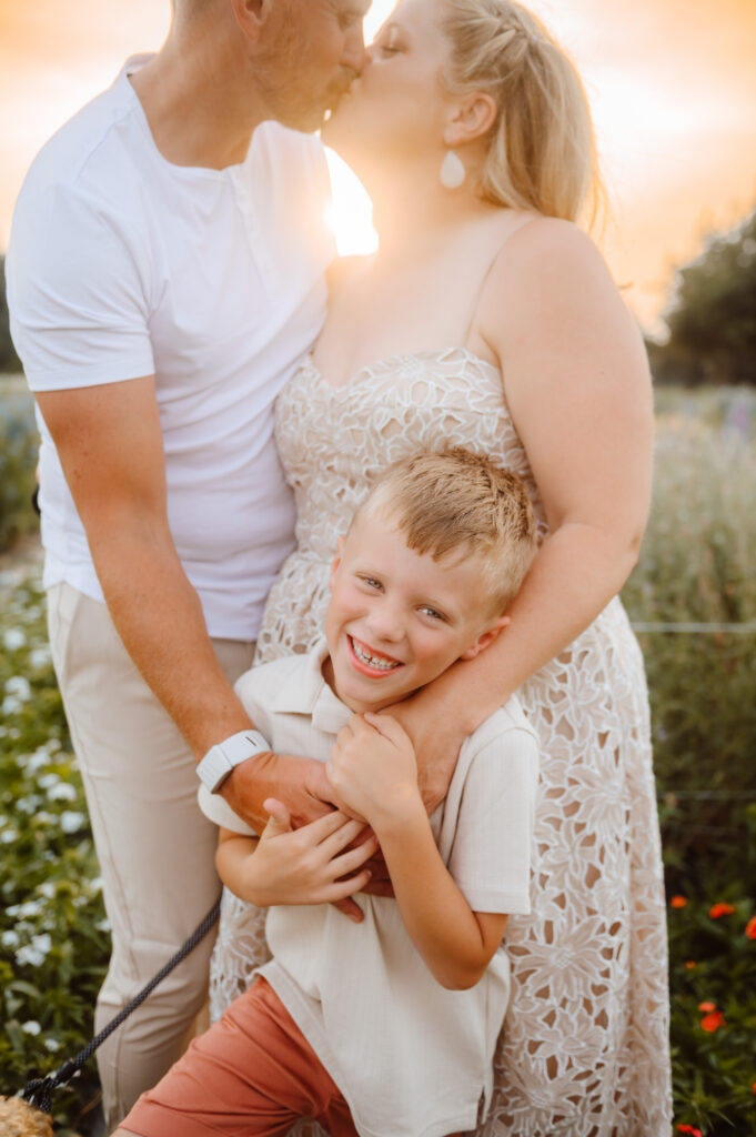 parents tickling their giggling son while sharing a kiss