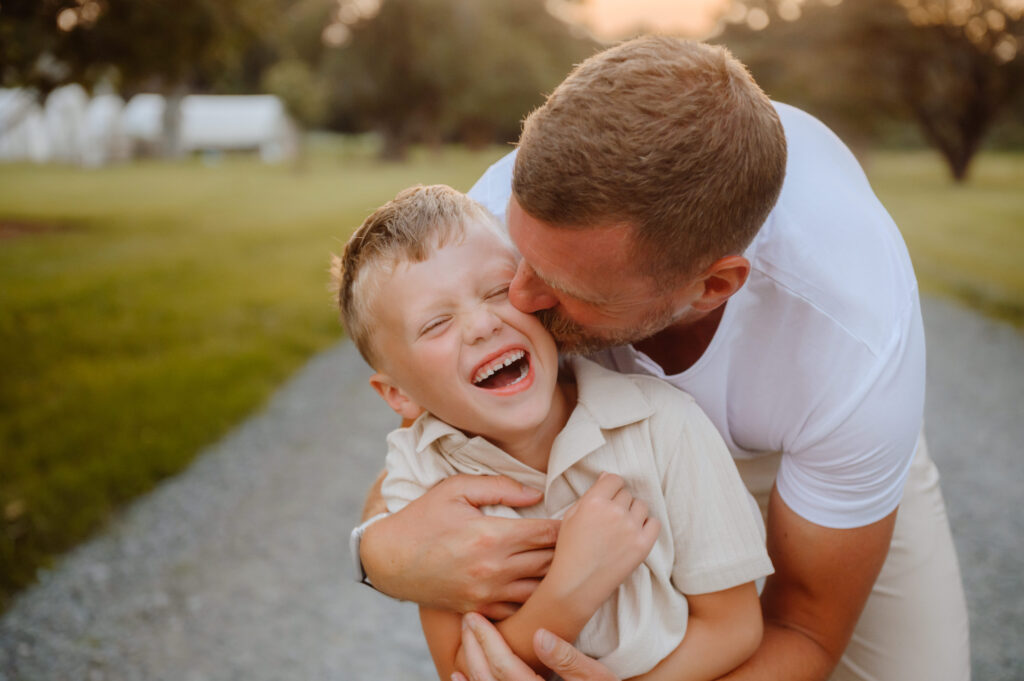 father smooches son on cheek while he giggles