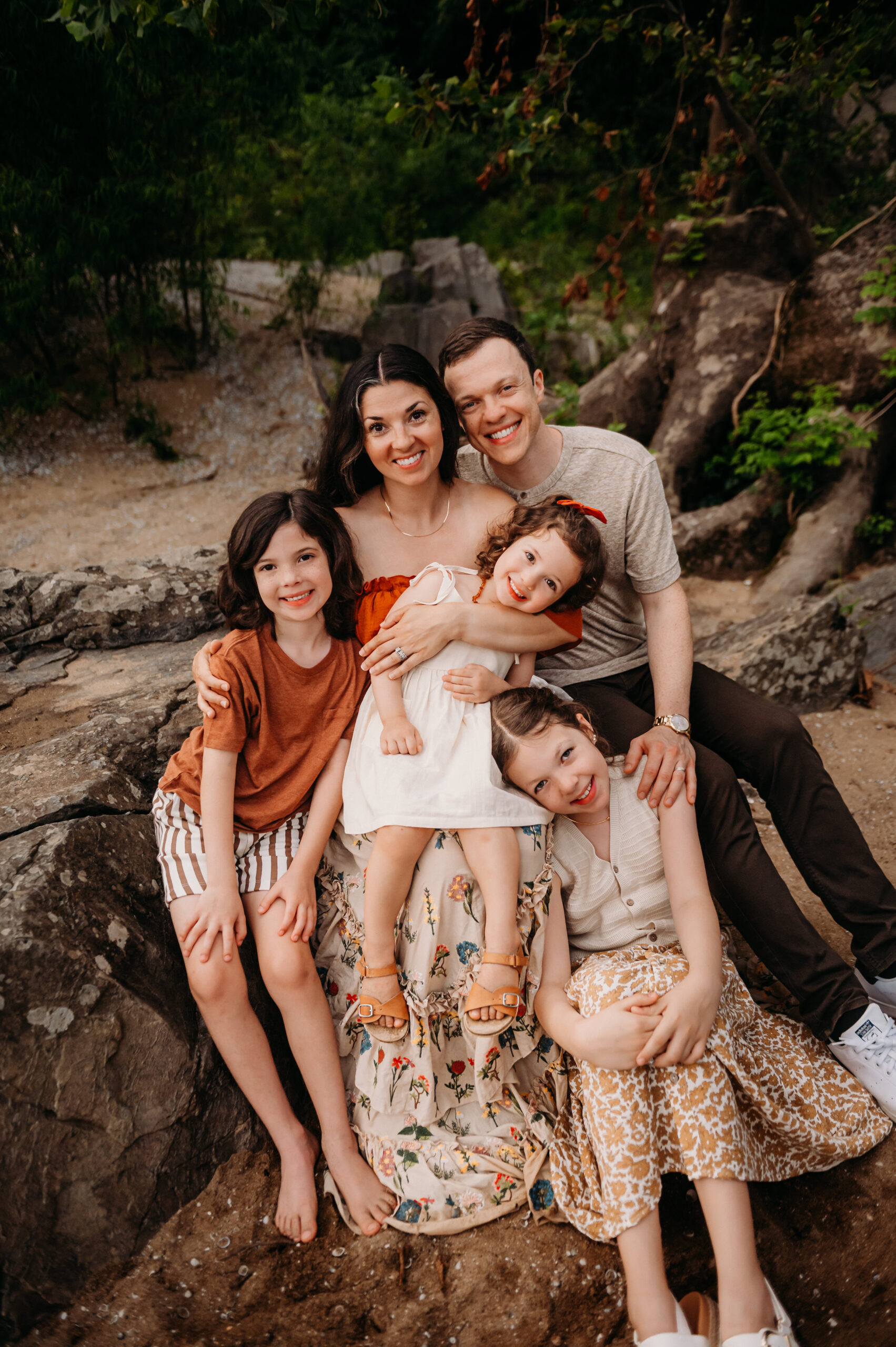 A beautifully styled family of five poses barefoot on the rocks at a scenic outdoor location in Maryland during golden hour. This image features natural light, joyful expressions, and thoughtfully coordinated outfits styled by Whitney of @styledbywi. Captured by Maryland family photographer Meredith Minor during a heartfelt summer model session.