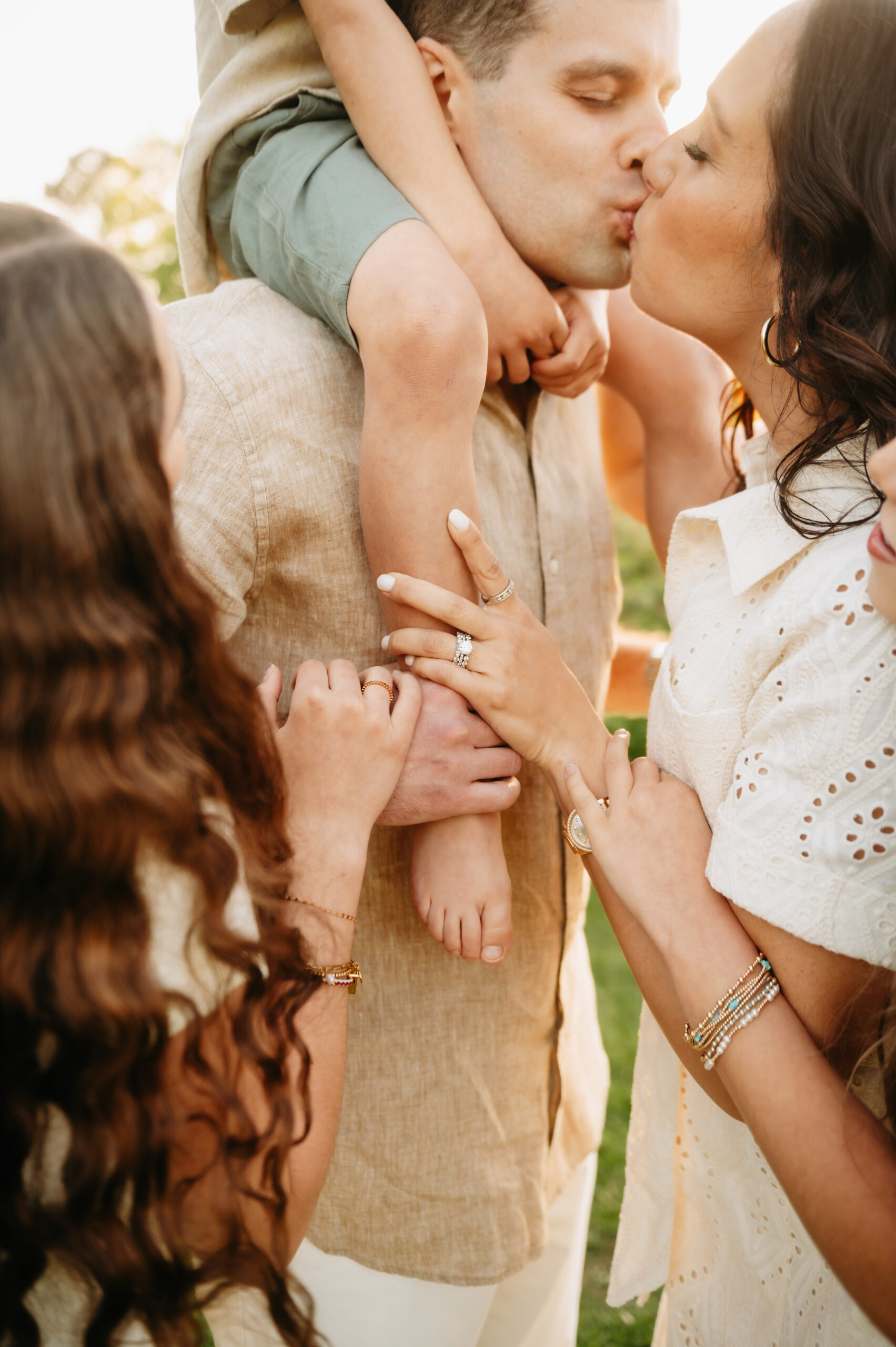 parents kissing with a child on dad's shoulders, hands of the whole family holding dad's wrist