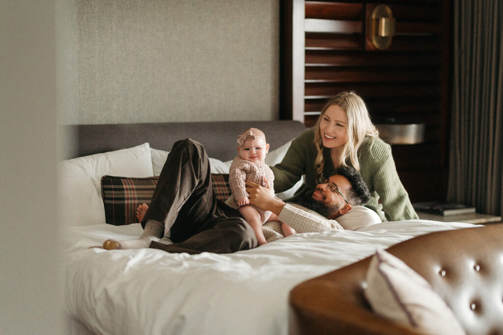 peek-a-boo image with parents on the bed. parents are smiling at their daughter, and the baby is looking at the camera with a smile