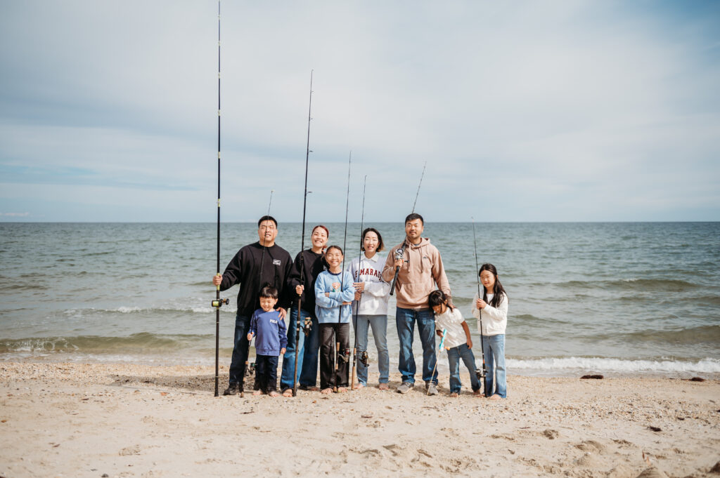 photo of two families of 4 each holding fishing poles with their backs to the cheseapeake bay, they are candid but it has a timeless and nostalgic essence to the image, the children are being silly and losing interest in the photo