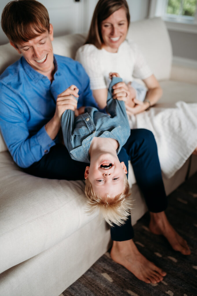 candid photo of a father dipping his son while sitting on a living room couch. 