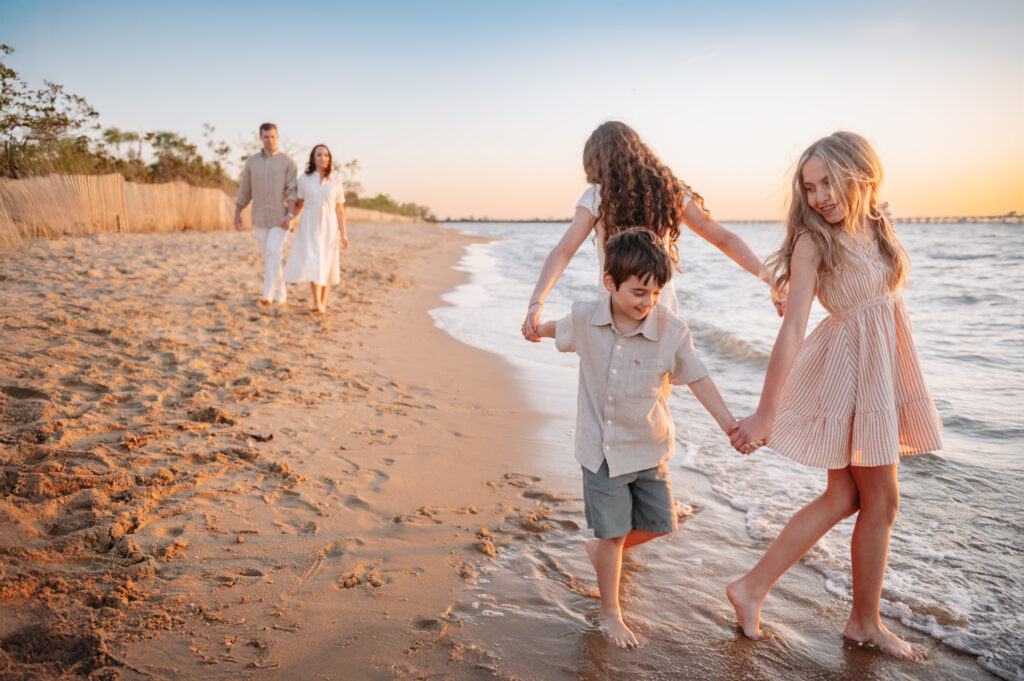 right front foreground, 3 kids play ring around the rosie, with parents in the back left distance admiring their kids as they walk toward them. parents are intentionally out of focus