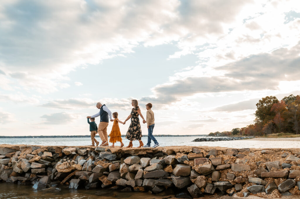 Family of five walks along a jetty with a big blue sky full of puffy clouds behind them