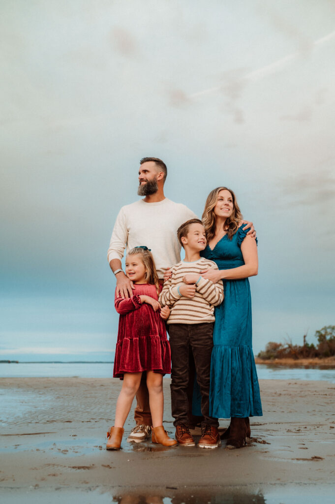 Family of four standing together on an eastern shore beach with a dramatic cloudy sky during a fall photography session