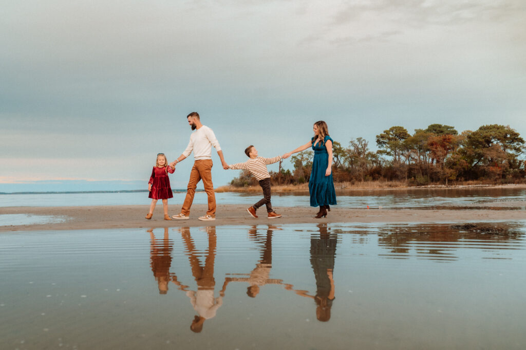 Family of four holding hands and walking along a sandy beach during a fall family session on Maryland's Eastern Shore
