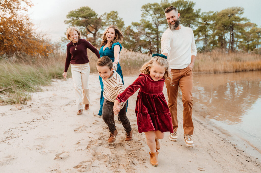 Extended family laughing and running together along a sandy path during an outdoor family session