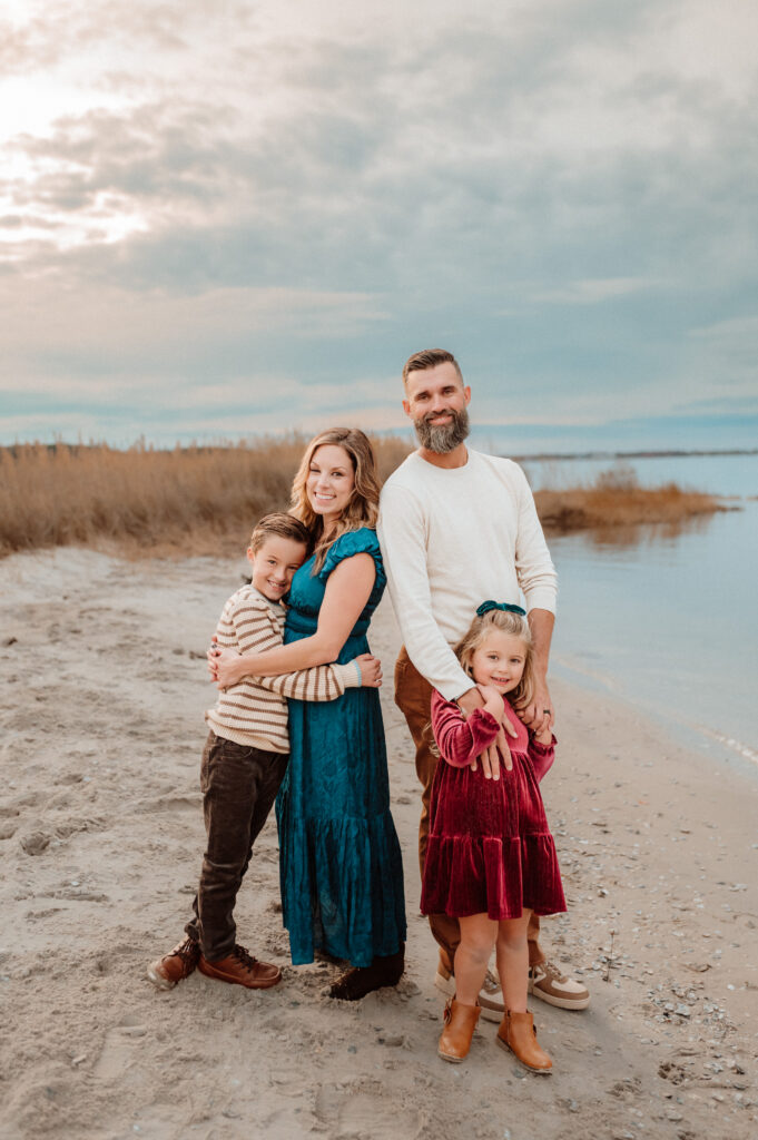 Two kids hugging their parents on a sandy beach during a fall family photography session