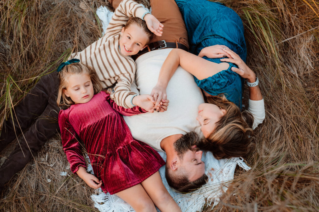 Overhead view of a family of four lying in a circle in tall coastal grass during a fall session with an Annapolis family photographer