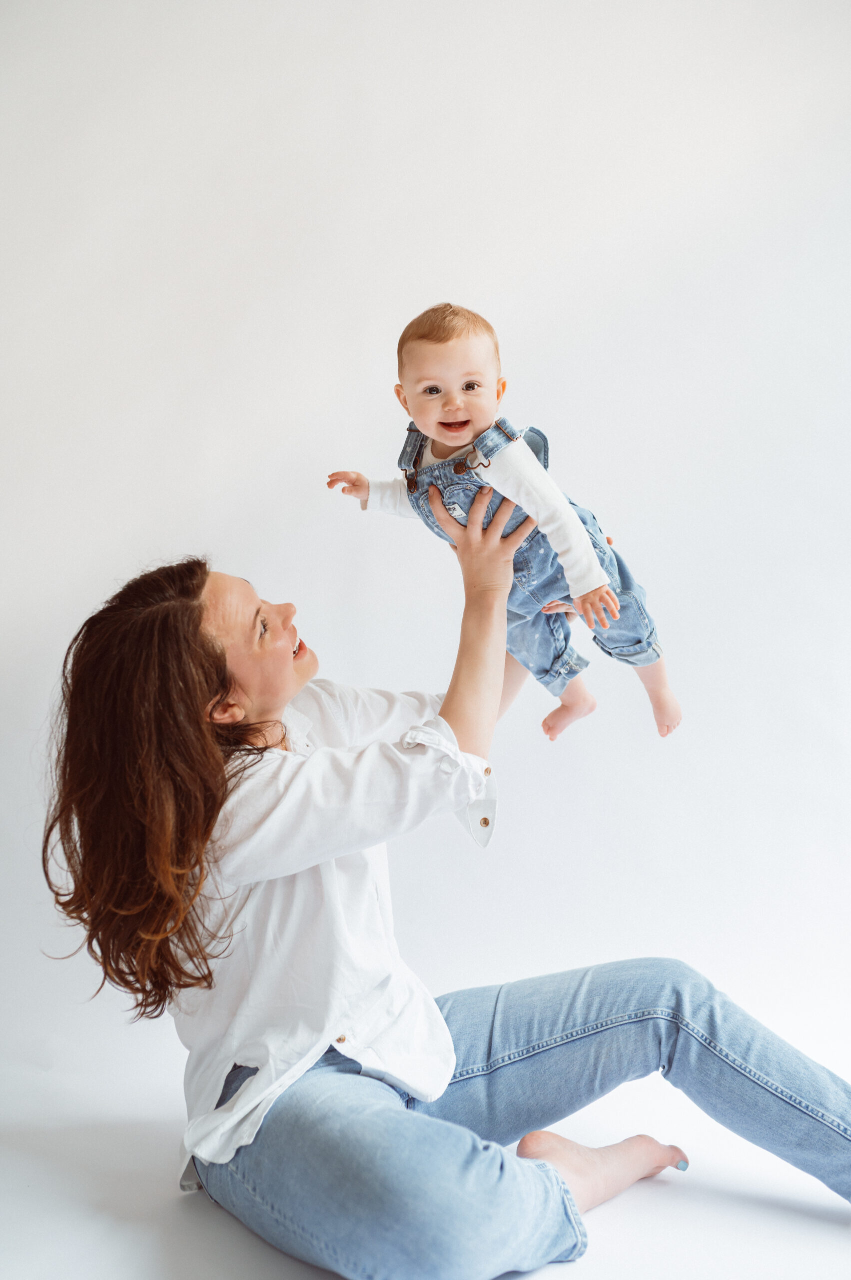 Mother holding baby in the air on a white backdrop in a studio setting